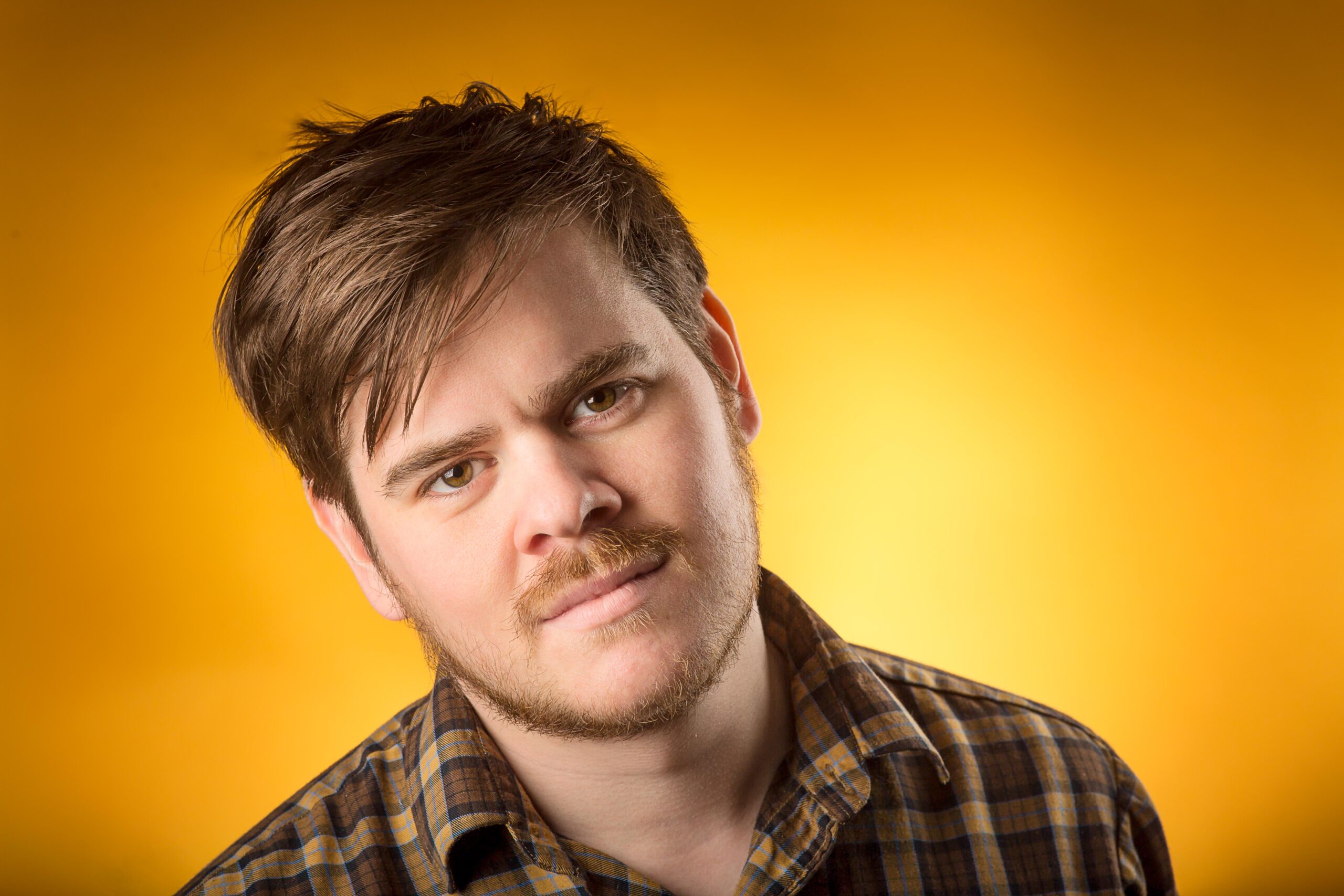 Self-portrait of Chad from Kirvan Photography + Film, wearing a brown plaid shirt with an orange background.