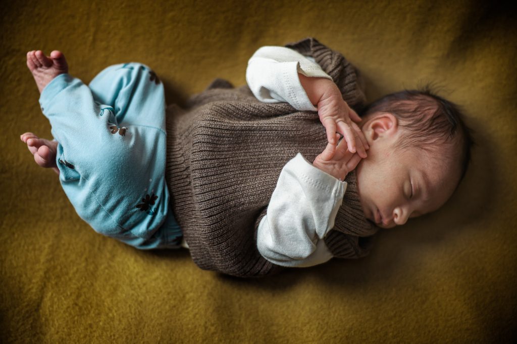 Top-down shot of newborn baby Elaahi lying on a soft yellow backdrop during a baby photoshoot at Kirvan Photography + Film’s Thunder Bay studio.