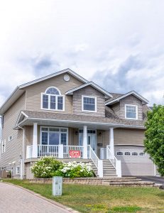 Facade of a beautiful brick house with massive windows, a garage, and white finishing in Thunder Bay, captured for property listing.