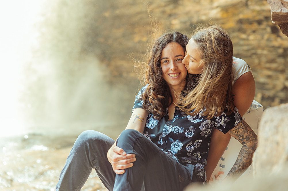Sam giving Jess a kiss on the cheek in front of a waterfall at Wolf River Falls, Thunder Bay.