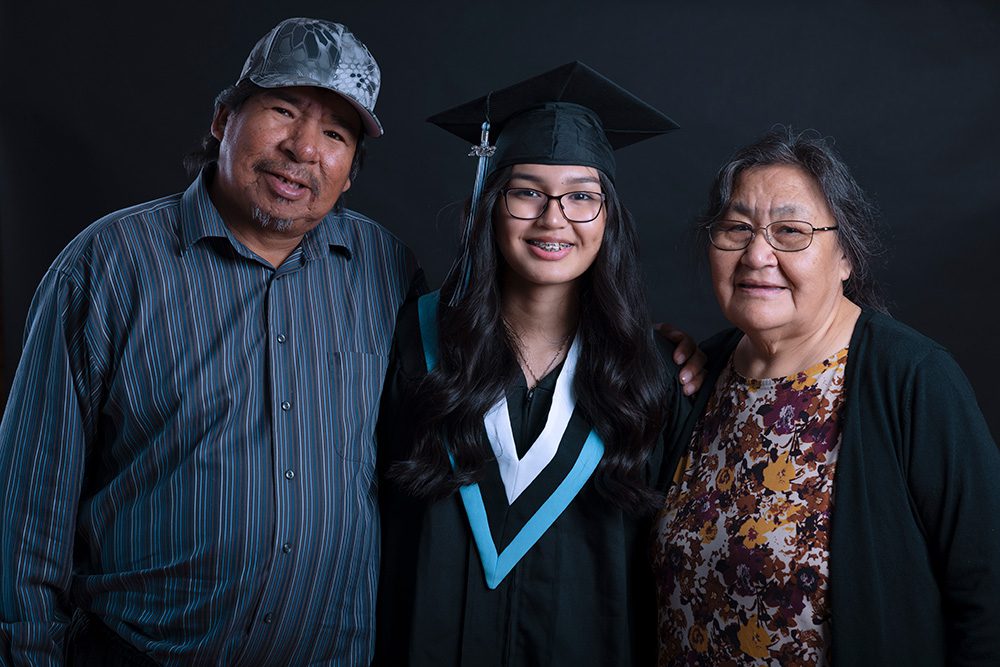 Young Indigenous graduate with family on black backdrop