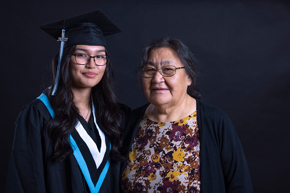 Young Indigenous graduate with her mother on black backdrop