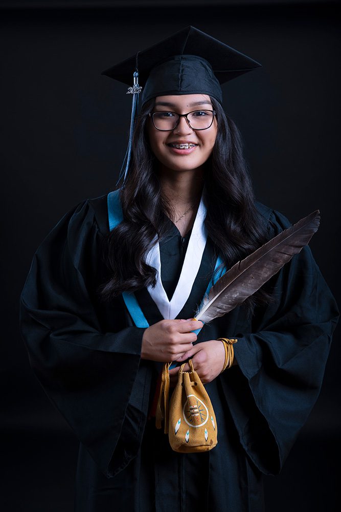 Young Indigenous graduate holding her medicine bag on black backdrop