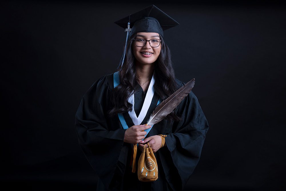 Young Indigenous graduate holding her medicine bag in landscape format on black backdrop