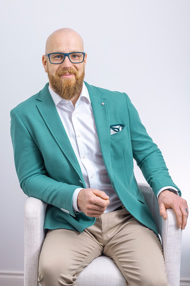 Jonathan from Royal LePage sitting in a high-top chair, smiling brightly while wearing a teal jacket and khaki pants.