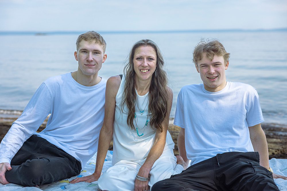 Sarah sits on a blanket at the beach with her two sons, smiling together in front of Lake Superior during their family photo session—captured through Photography Gift Cards in Thunder Bay.