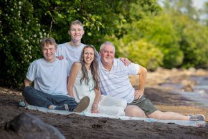 Sarah, her husband, and their two sons lay together on a blanket with the full stretch of the beach and Lake Superior behind them—captured using Photography Gift Cards in Thunder Bay.