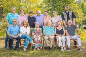Alt Text: Joyful multi-generational family smiling brightly at the camera during a summer portrait session in Thunder Bay.