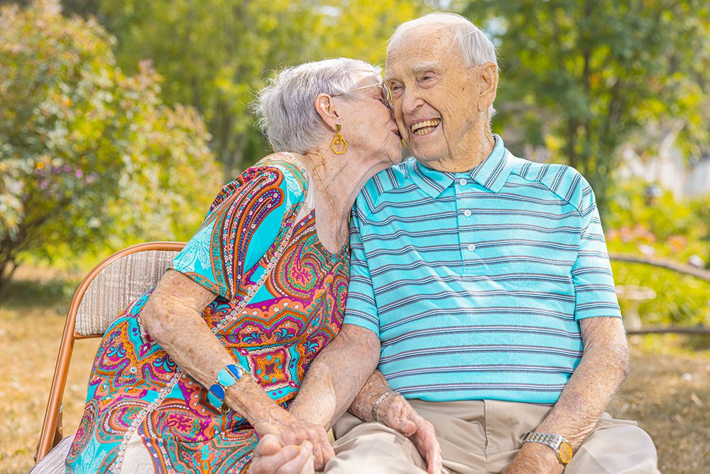 Norma giving her husband a sweet kiss on the cheek during their summer family portrait session in Thunder Bay.