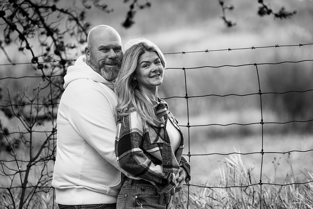 Husband and wife standing near a wooden fence post during family photo session