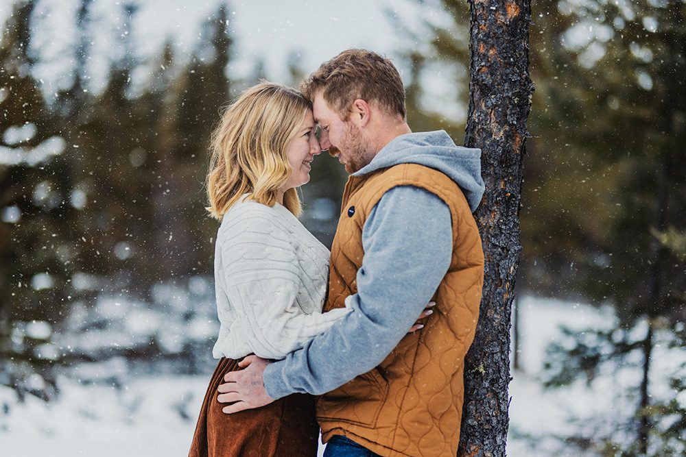 Winter engagement photo of Mac and Steph leaning against a tree and gazing lovingly into each other's eyes during their photo session