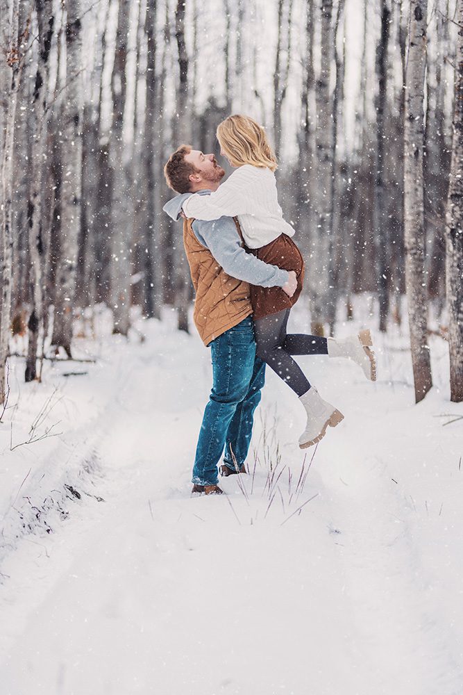 Winter engagement photo of Mac lifting Steph in a romantic pose during their Thunder Bay session.