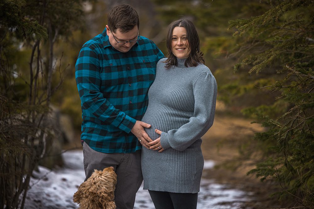 Sophie smiles at the camera while Jeff lovingly gazes down at her baby bump as they stand together in a wooded area at Chippawa Park, Thunder Bay.