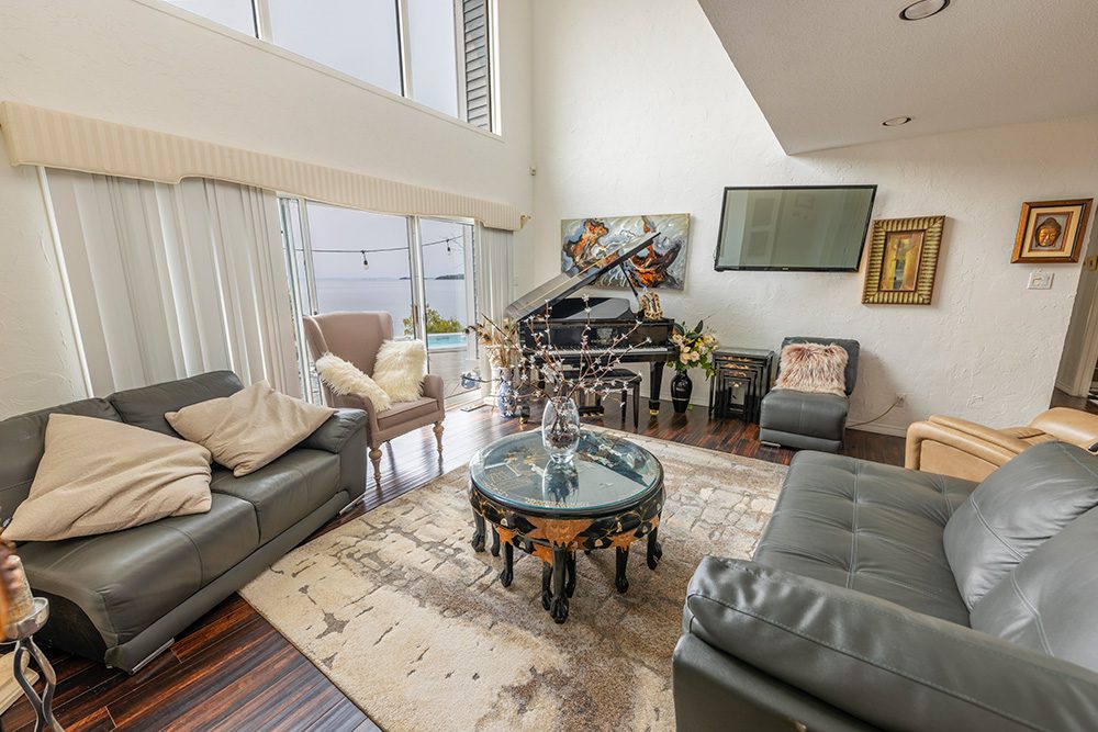Luxury modern living room with gray leather furniture, glass coffee table, fireplace, and high ceilings