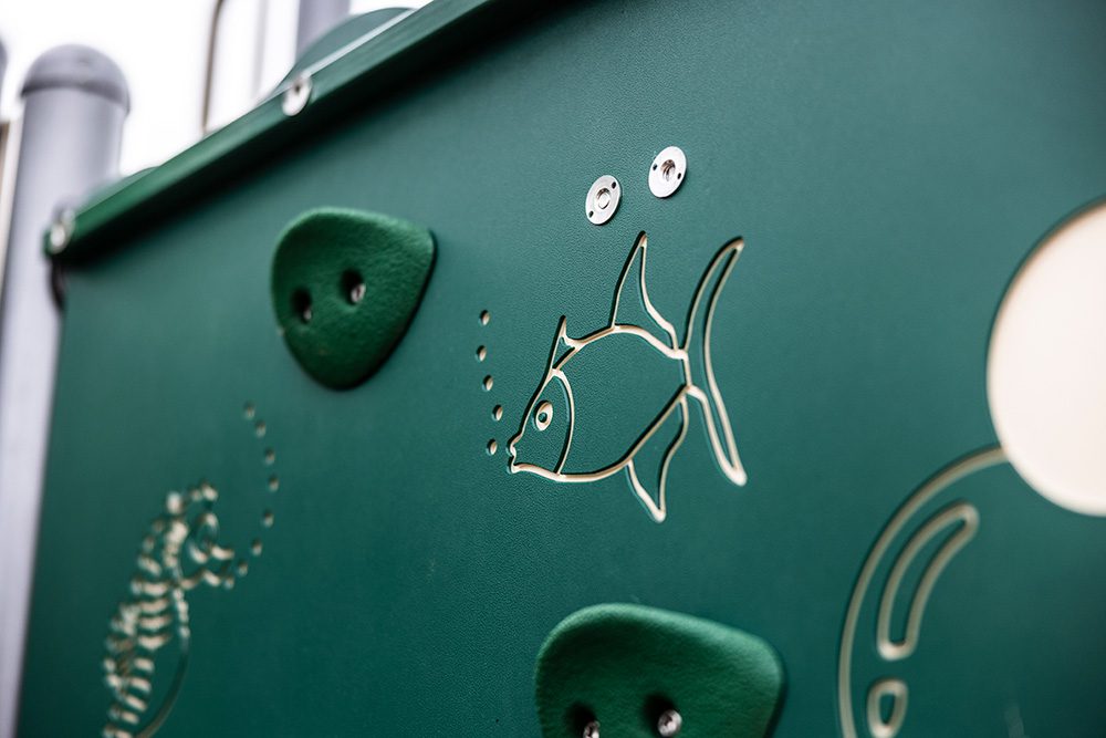 Close-up of green playground equipment featuring embossed fish design and climbing holds