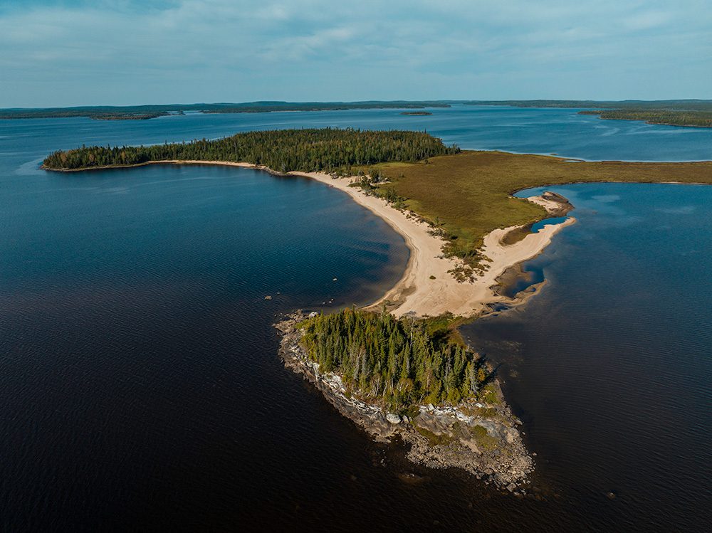 Aerial view of pristine wilderness peninsula with sandy beaches, dense forest, and crystal clear blue waters dotted with small islands