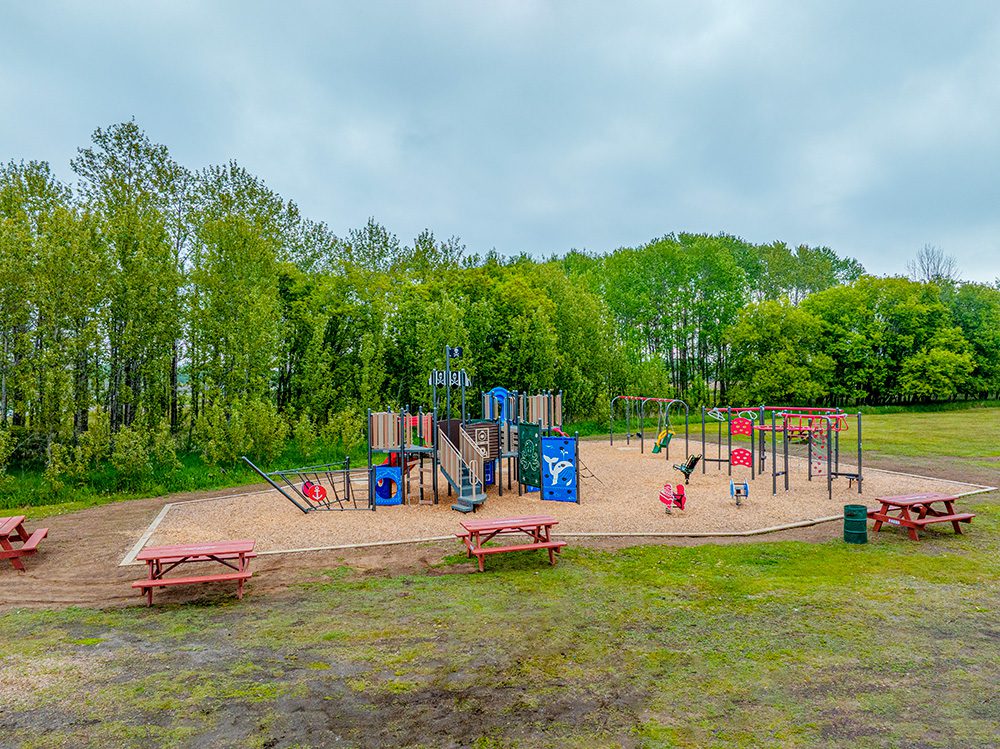 Full playground area showing pirate ship structure, swings, picnic tables, and open field surrounded by trees