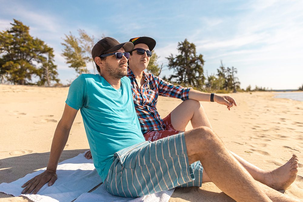 A couple relaxing on a sandy beach under a clear blue sky, sitting on towels and enjoying the sunshine together.