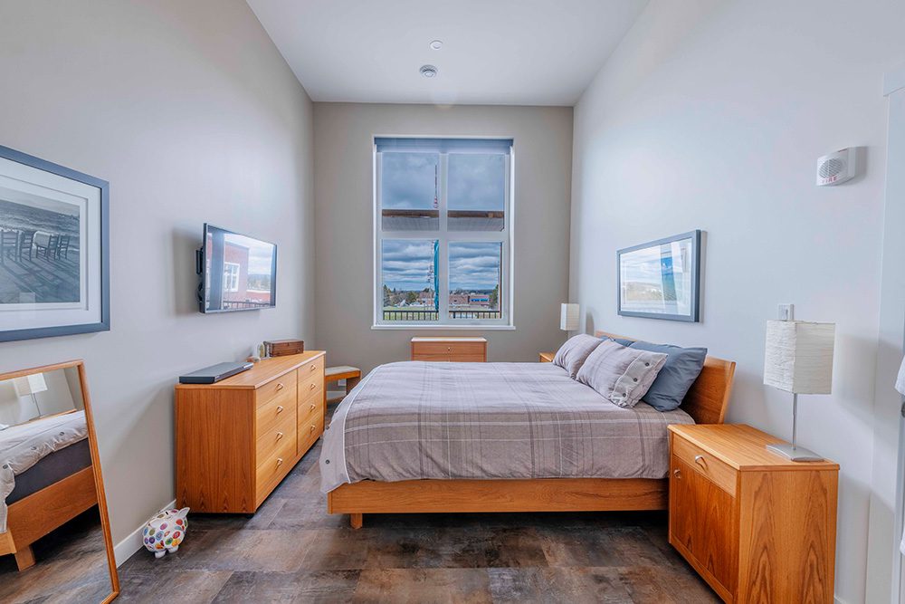 Modern bedroom with mid-century teak furniture, platform bed, gray bedding, wall-mounted TV, and window overlooking city views