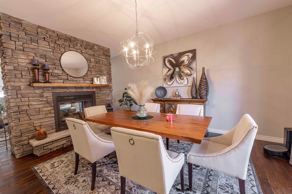 Elegant dining room with stone fireplace, wooden table, cream upholstered chairs, modern chandelier, and decorative wall art