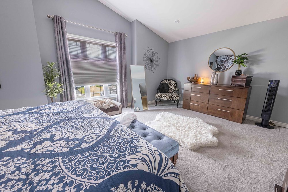 Spacious master bedroom with gray walls, blue and white patterned bedding, wood dresser, zebra print accent chair, and white shag area rug
