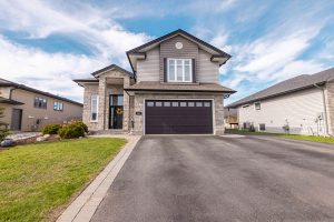 Modern two-story home with stone and vinyl siding, dark garage door, and decorative wreath on front door in residential neighborhood under dramatic cloudy sky