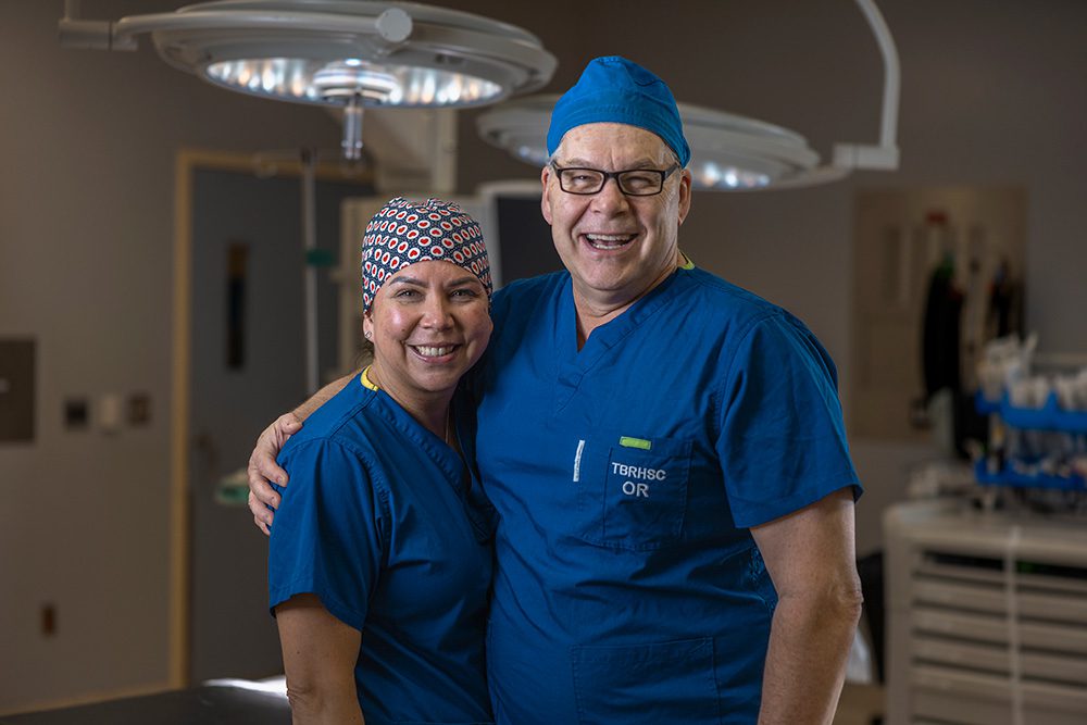 Two smiling surgeons in blue scrubs standing together in an operating room.