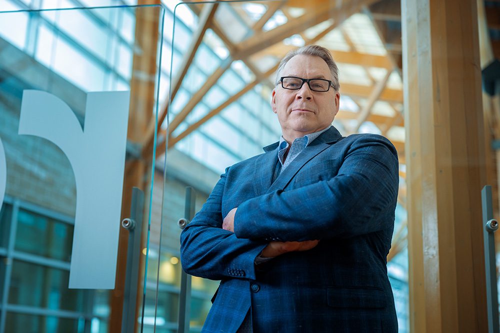 Professional man in a tailored blue suit standing with arms crossed in a modern, architecturally designed interior.