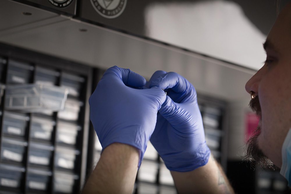 Tattoo artist wearing blue gloves preparing piercing jewelry in a professional studio workspace.