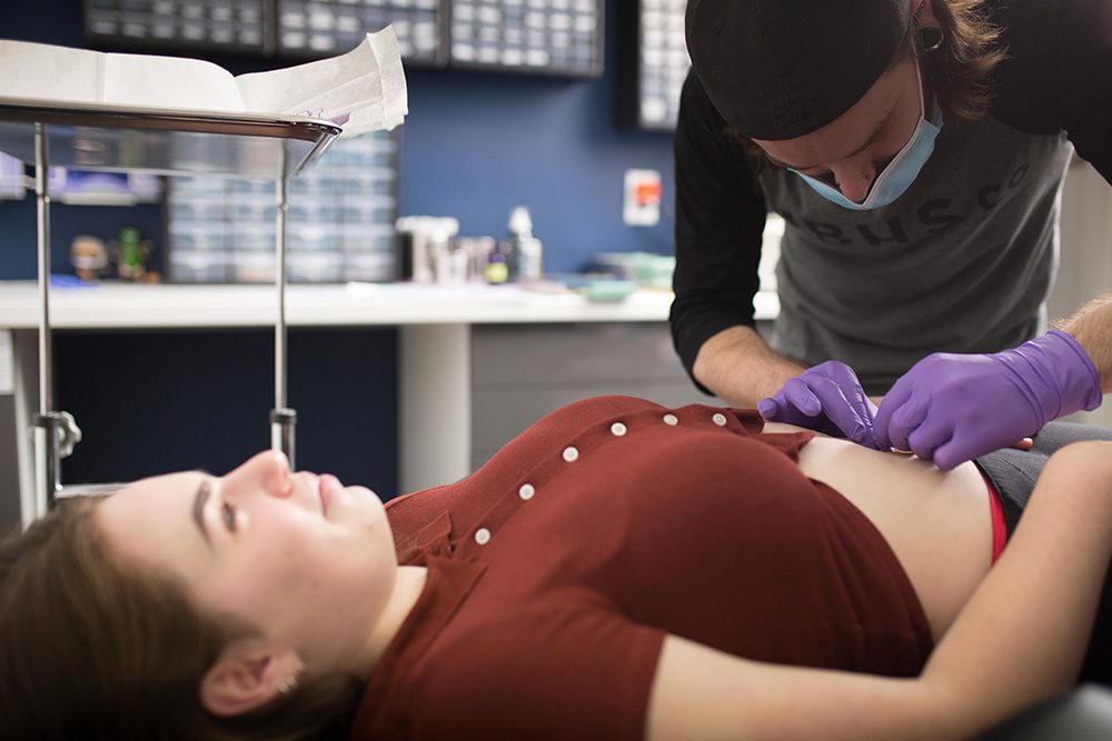 Tattoo artist performing a navel piercing on a client in a clean tattoo studio.