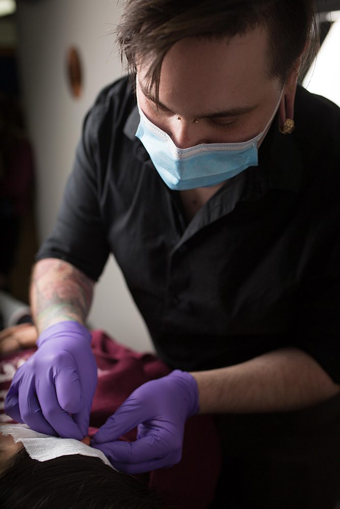 Piercer in mask and gloves preparing piercing equipment during procedure at Identity Tattoo and Piercing