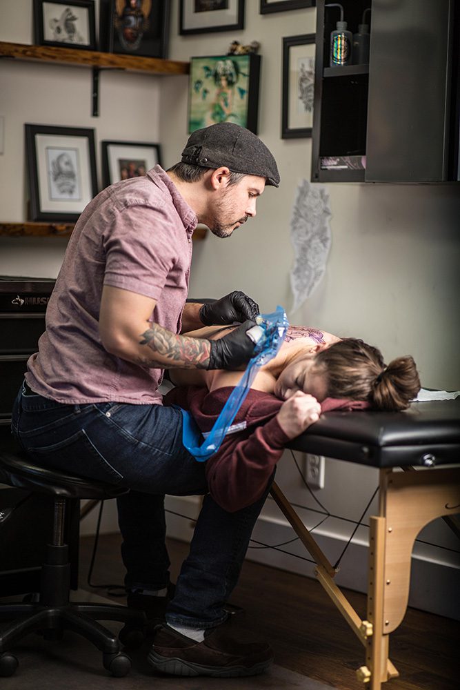 Tattoo artist working on client's back tattoo at Identity Tattoo and Piercing studio