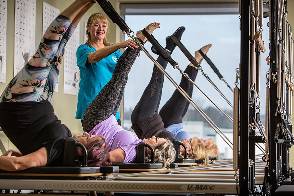 Pilates instructor smiling while guiding clients through inverted reformer exercises