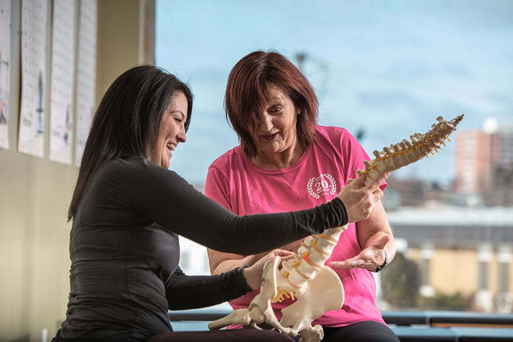 Pilates instructor and client examining anatomical spine model in fitness studio