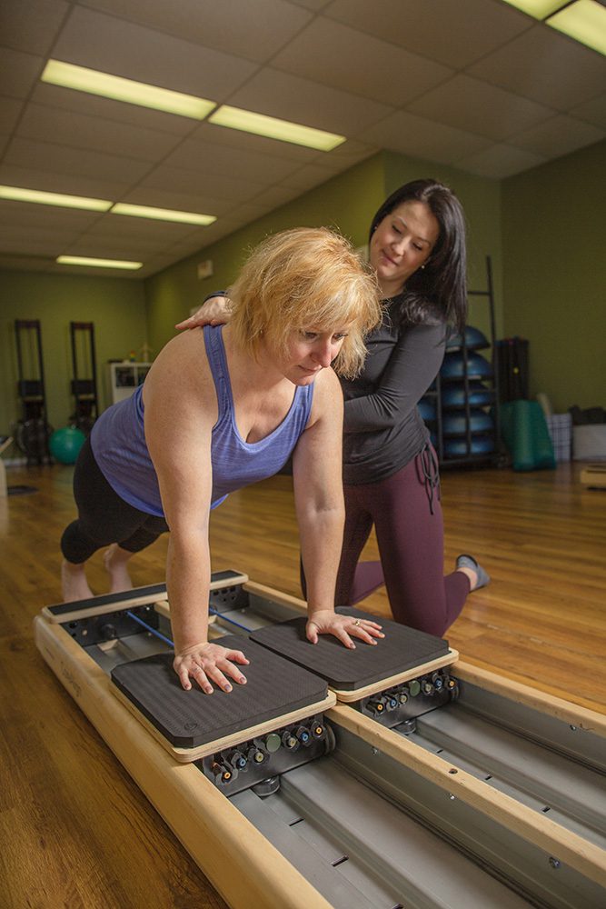 Woman doing plank exercise on Pilates reformer with instructor providing support