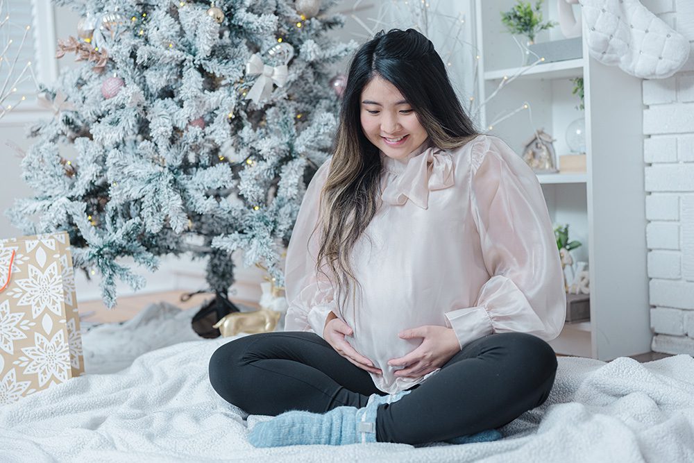 Pregnant woman looking down at baby bump peaceful holiday maternity portrait