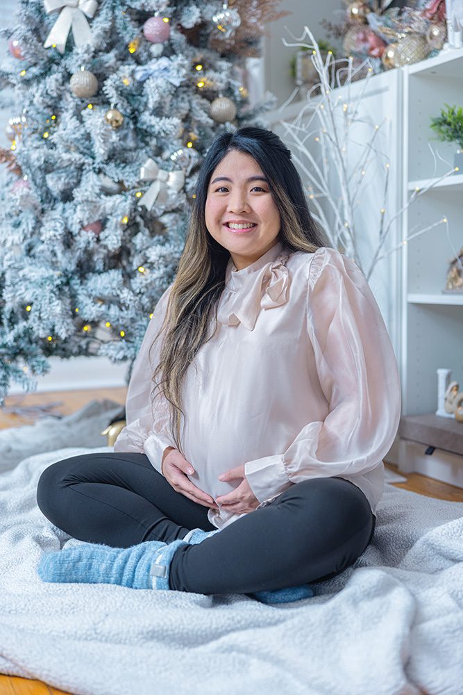 Smiling pregnant woman sitting cross-legged cradling baby bump Christmas setting