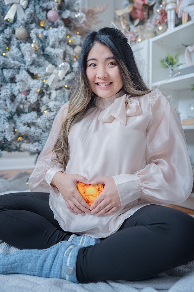 Pregnant woman sitting cross-legged holding heart-shaped light on baby bump