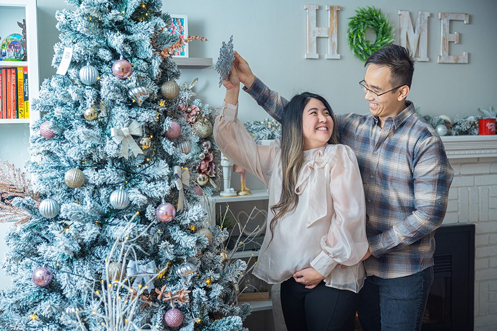 Pregnant woman holding star over flocked Christmas tree with partner