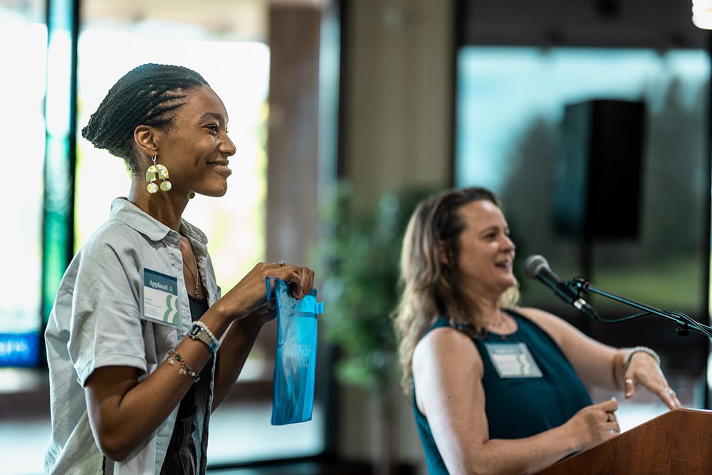 Two female presenters at podium with one holding branded gift bag