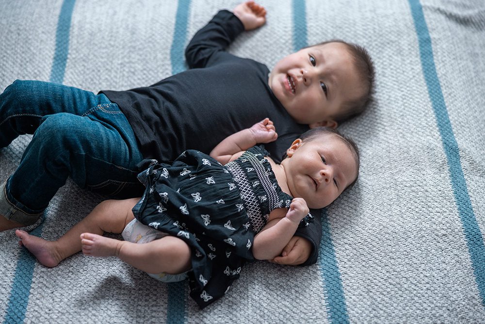 Smiling toddler lying with sleeping newborn baby studio portrait