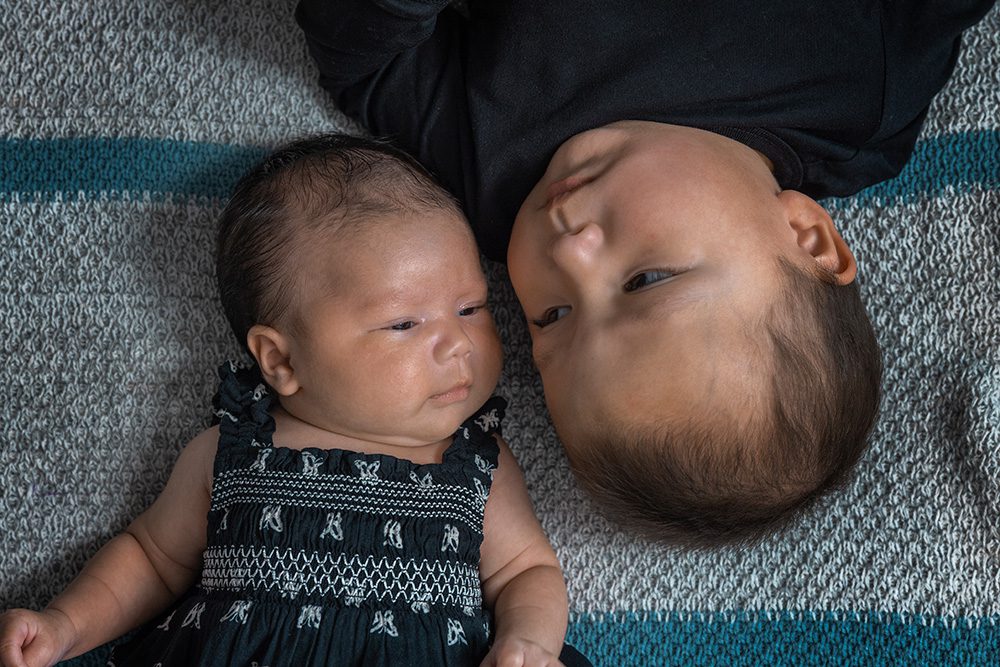 Newborn baby and toddler lying side by side heads together overhead view
