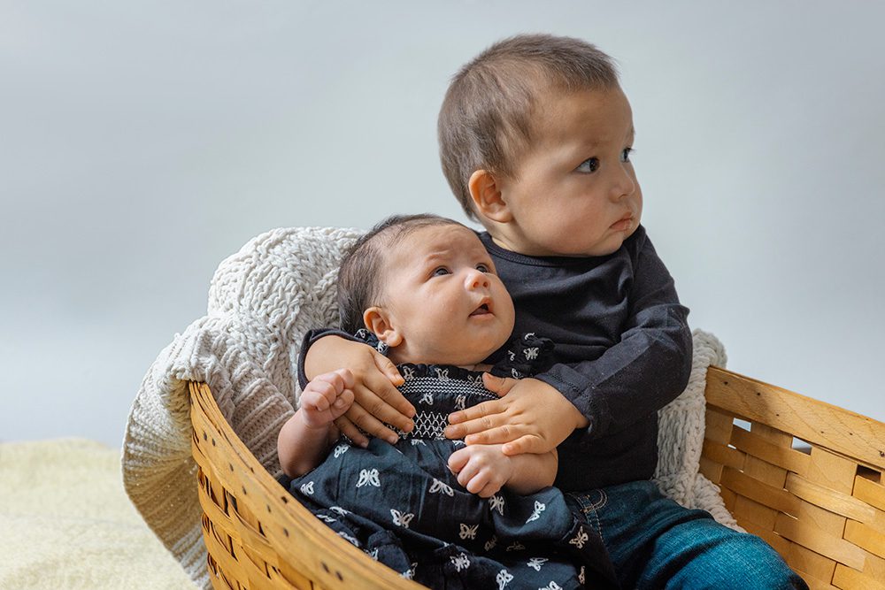 Toddler and newborn baby together in wicker basket tender sibling moment