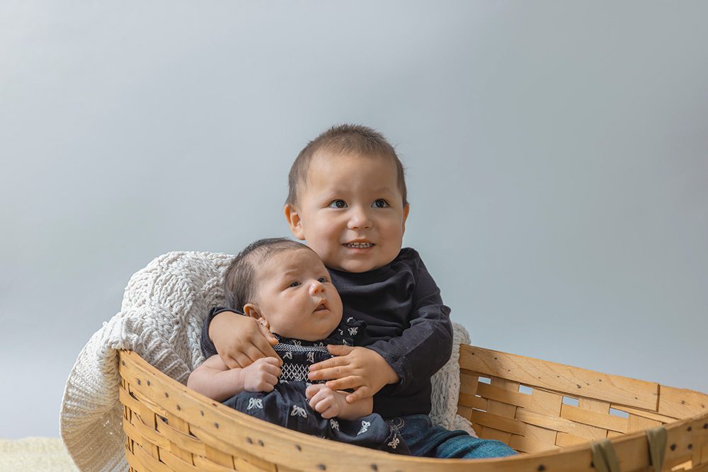 Smiling toddler holding newborn baby in basket looking at camera