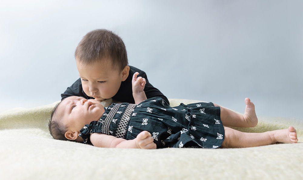Toddler boy kissing newborn baby sister lying on fur blanket