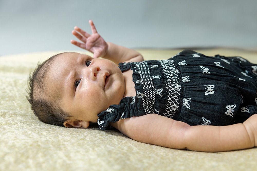 Alert newborn baby in butterfly dress lying on cream fur studio