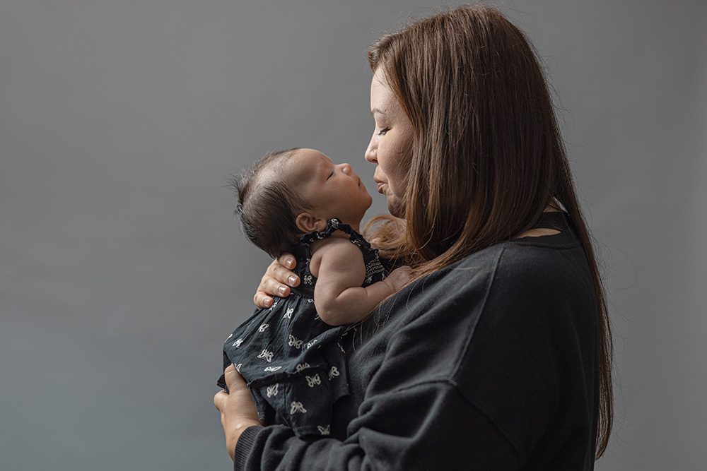 Mother kissing newborn baby tenderly studio portrait side profile
