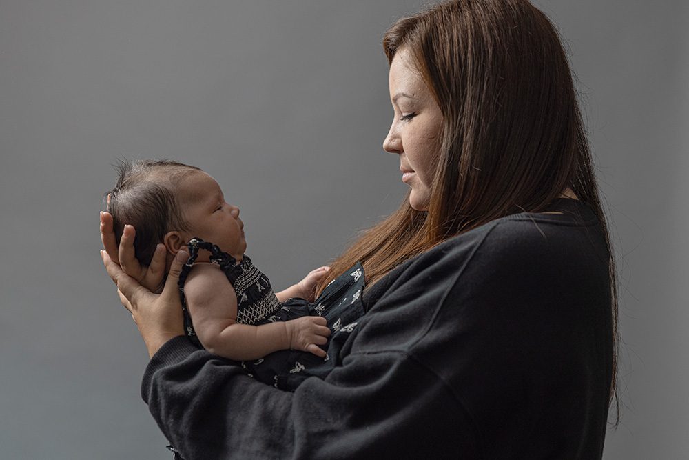 Mother in black holding newborn baby face to face tender moment studio