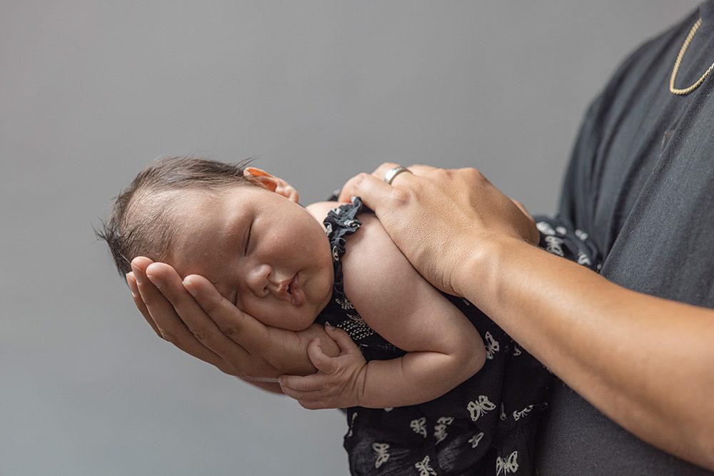 Mother cradling newborn baby in hands close up studio portrait