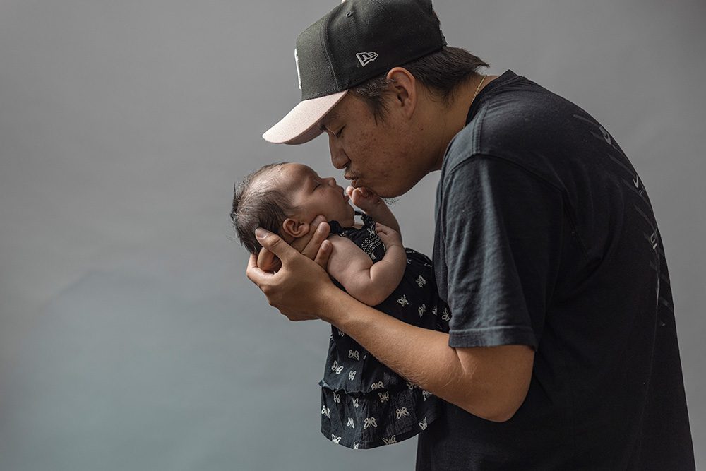 Father in Yankees cap tenderly holding newborn baby close to face studio portrait
